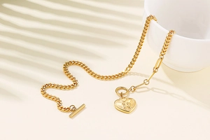 Detail of a golden heart pendant necklace with T-bar clasp on a beige surface