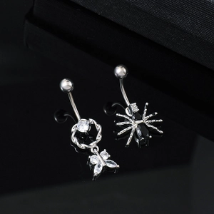 Close-up of butterfly and spider belly rings with cubic zirconia on black surface