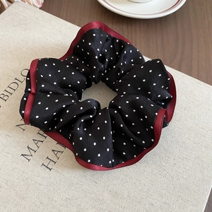Detailed view of a black polka dot scrunchie with burgundy ribbon edge on a linen book