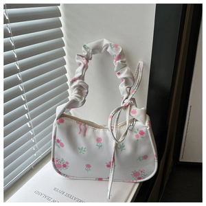 Detail of floral canvas handbag with pink roses, ruffled handle, and bow on a book