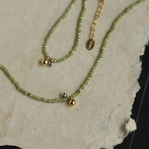 Olive green beaded necklace with gold and silver steel accents on textured paper