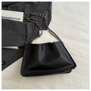 Detail of black pleated cloud bag featuring a silver woven chain strap on fabric
