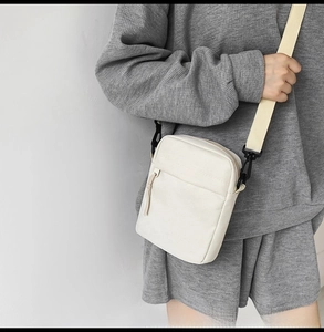 Close-up of cream canvas messenger bag with adjustable strap and metal hardware