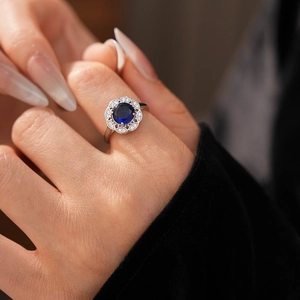 Close-up of blue zircon diamond flower ring with silver band on a model finger