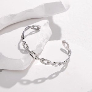 Dettaglio dell'elegante bracciale rigido a catena su un supporto in pietra bianca minimalista