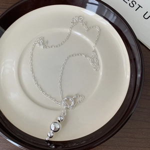 Detail of silver beaded necklace with four different sized spheres on ceramic tray
