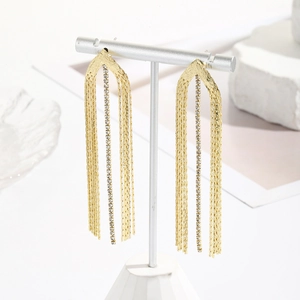 Detail shot of long gold tassel earrings with sparkling white rhinestones on T-stand