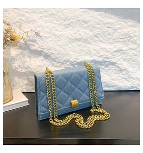 Close-up of blue denim quilted bag featuring gold metal chain and square buckle detail