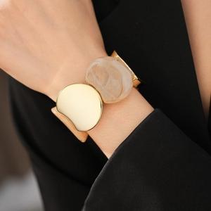 Macro shot of chunky gold metal and white marble resin cuff bracelet on a model