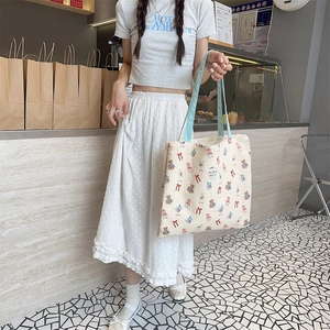 Detail view of a cream canvas tote bag with bear print and light blue handles on model