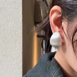Gros plan d'une boucle d'oreille géométrique irrégulière en argent mat sur modèle