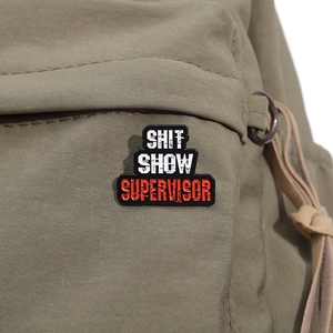 Funny Shit Show Supervisor enamel badge pinned on a khaki canvas bag background