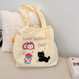 Detail of cute embroidered cat and milk patterns on beige canvas shoulder tote bag