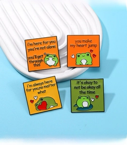 Detailed view of four green frog enamel badges with inspirational quotes on a ceramic tray
