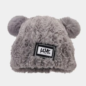 Détail du bonnet en tricot gris avec doubles pompons doux et un écusson LOVE