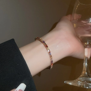 Close-up of a rose gold bangle featuring colorful rectangular crystals in a rainbow pavé setting
