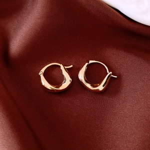 Detailed close-up of rose gold pleated oval hoop earrings on dark red satin fabric