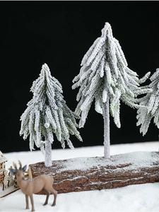 Miniature snow-flocked green pine trees on a natural wood base for Christmas tabletop decor