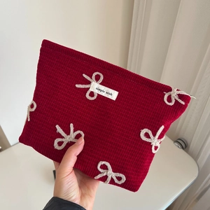 Detail of red corduroy makeup bag with beige bows and a woven simple wish label