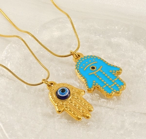 Detail of Hamsa Hand pendants with blue evil eye on gold snake chains over textured glass