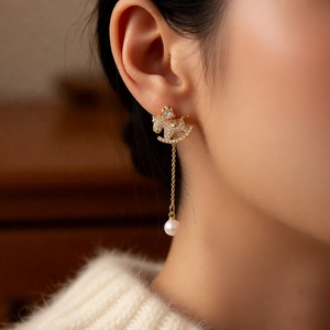 Detailed close-up of 18k gold rocking horse earring with dangling pearl tassel on model