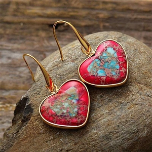 Close-up of bohemian heart-shaped earrings with magenta emperor stone and golden hooks