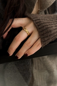 Detailaufnahme des goldfarbenen Rings mit Rautenmuster an einem Finger mit Strickpullover