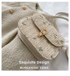 Detail of floral embroidery on a straw shoulder bag with a gold metal lock and leather strap