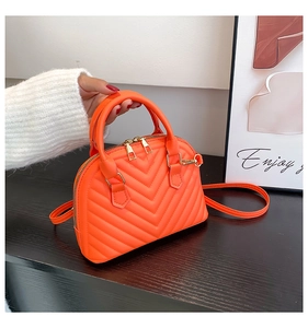 Detail of bright orange shell bag with V-shaped quilting and gold metal zipper hardware