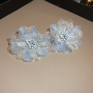 Close-up of light blue mesh flower earrings with white pearl centers on textured base
