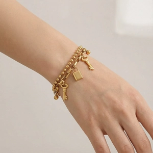 Close-up of double-layered gold bracelet featuring bead chain, padlock and key charms