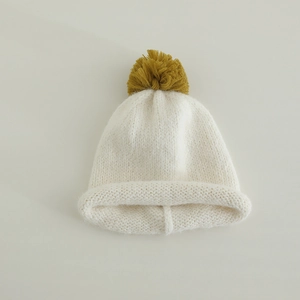 Close-up of knit texture on cream beanie with a ginger yellow yarn pom pom