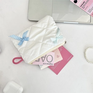 Detail of white quilted makeup bag featuring blue plaid and green ribbon bows