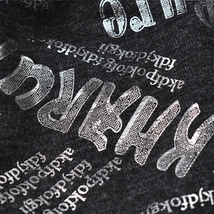 Close-up detail of a black knit beanie hat with silver metallic letter print patterns