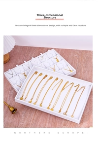Detailed view of white faux leather jewelry display trays showing necklaces on wood surface