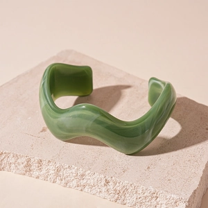 Detail of green wavy acrylic bangle with marble texture on natural stone pedestal