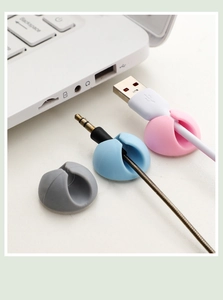 Close-up of pastel silicone cable organizers in pink, blue, and gray on a white desk