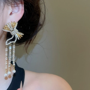 Detail of luxury bow pearl earrings with long zircon tassels on a female model