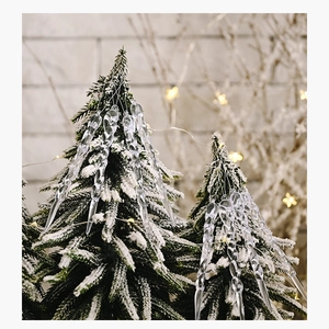 Macro shot of clear acrylic icicle ornaments hanging on a snowy Christmas tree branch