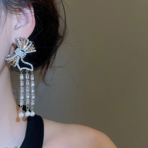 Close-up of bow tassel earrings with zircon and pearls worn by a model in soft light