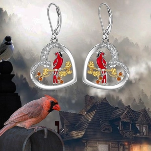 Detailed close-up of heart-shaped earrings with red enamel bird and crystal accents