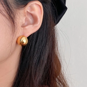 Close-up of polished gold spherical stud earrings on model for a minimalist modern look