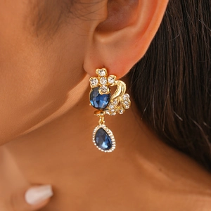 Macro detail of vintage gold floral earrings featuring navy blue teardrop crystal pendants