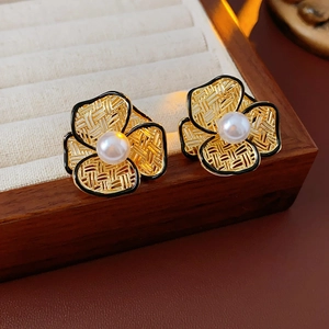 Close-up of gold-plated flower stud earrings with black enamel edges and center pearls