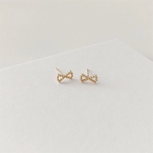 Detail of gold bow earrings featuring textured bead surface on a minimalist card
