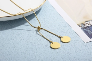 Detail of adjustable gold snake chain necklace with twin round pendant discs on blue surface