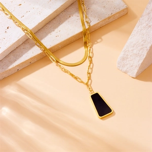 Gold layered necklace featuring snake chain and black trapezoid pendant on stone