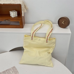 Close-up of floral embroidery on yellow canvas tote bag strap for commuter style