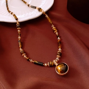 Close-up of vintage tiger eye stone pendant with golden metal accents on red silk
