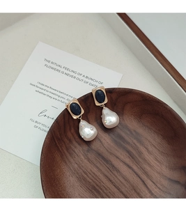Dettaglio orecchini vintage con perle barocche e pietre nere su vassoio di legno
